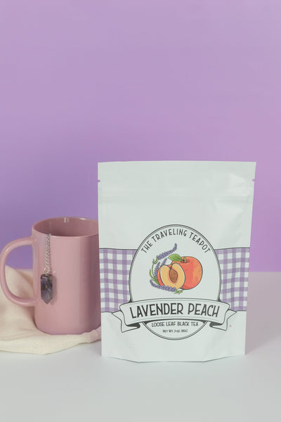 A retail bag of lavender peach black tea next to a pink mug with an amethyst tea infuser