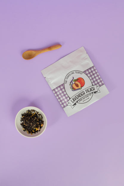 A bag of lavender peach black tea next to a cup of loose leaf leaves on a purple background