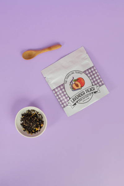A bag of lavender peach black tea next to a cup of loose leaf leaves on a purple background